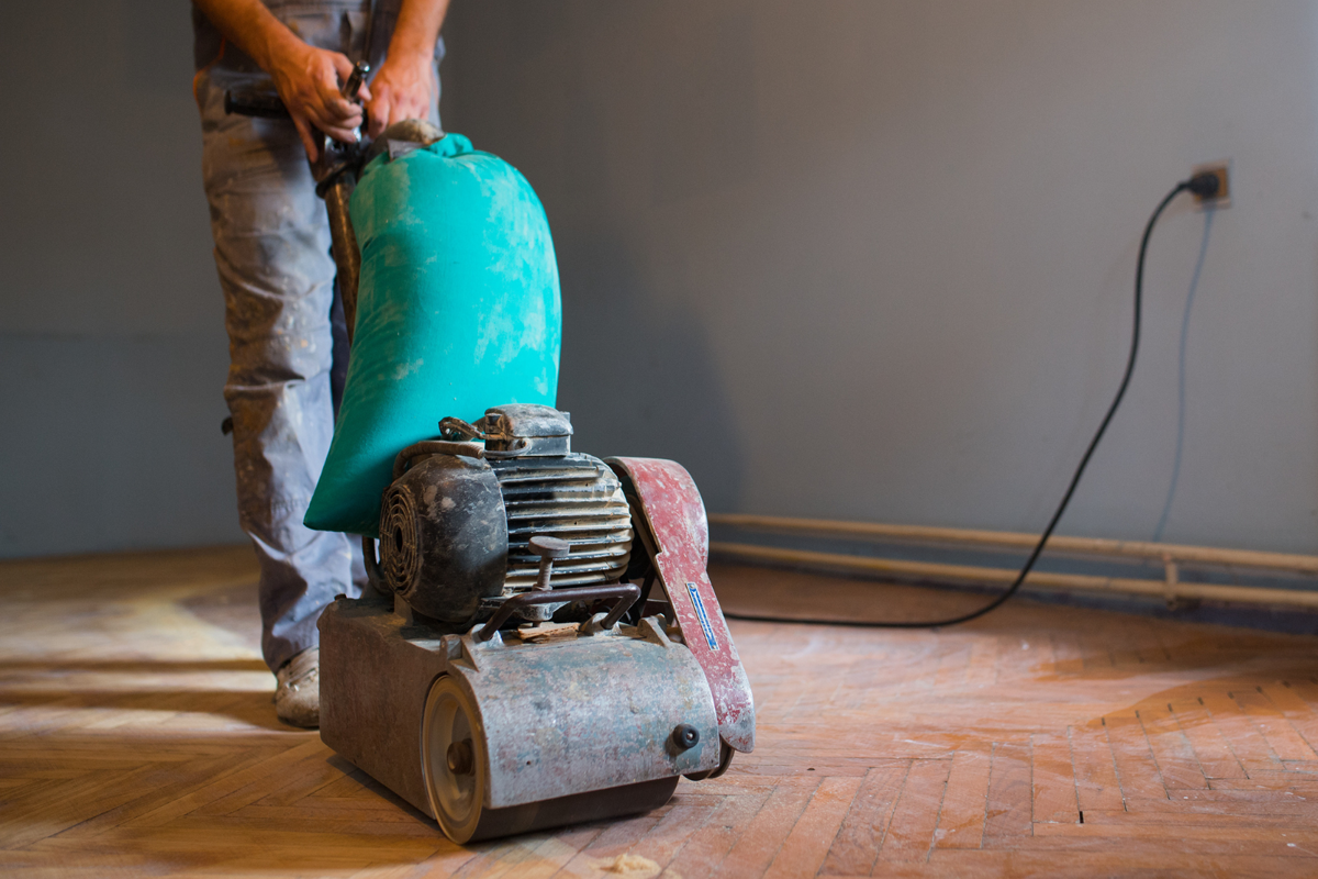 Een vakman herstelt een parketvloer door beschadigde delen professioneel te schuren en te behandelen